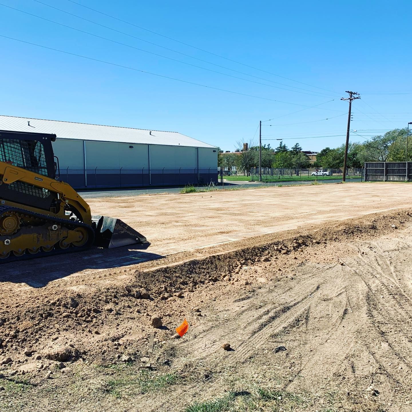 A small yellow bulldozer on a dirt lot in front of a building under a blue sky.