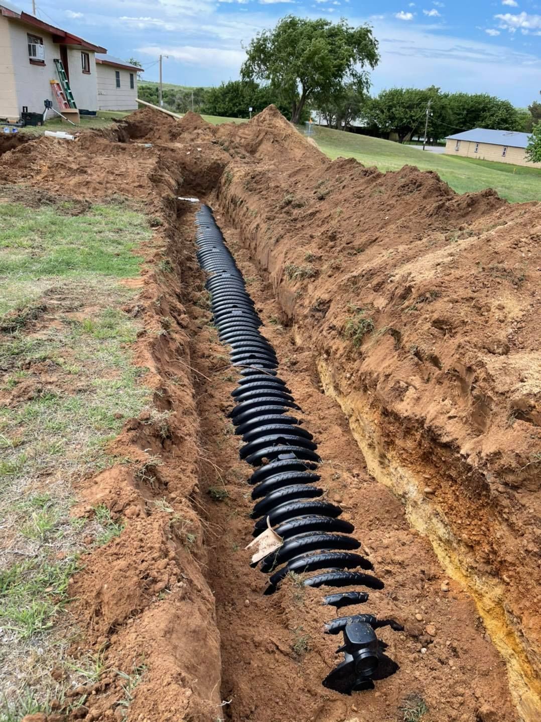 A deep trench with black septic system components installed in a yard.
