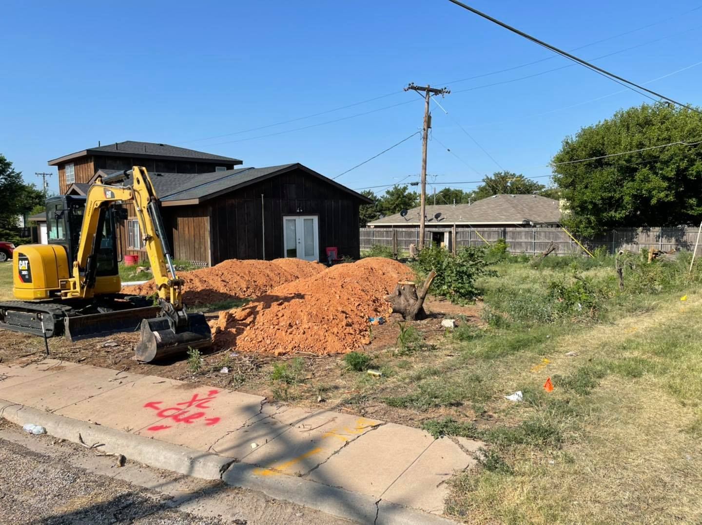 Yellow excavator digging on a construction site next to a dark house; sunny day.