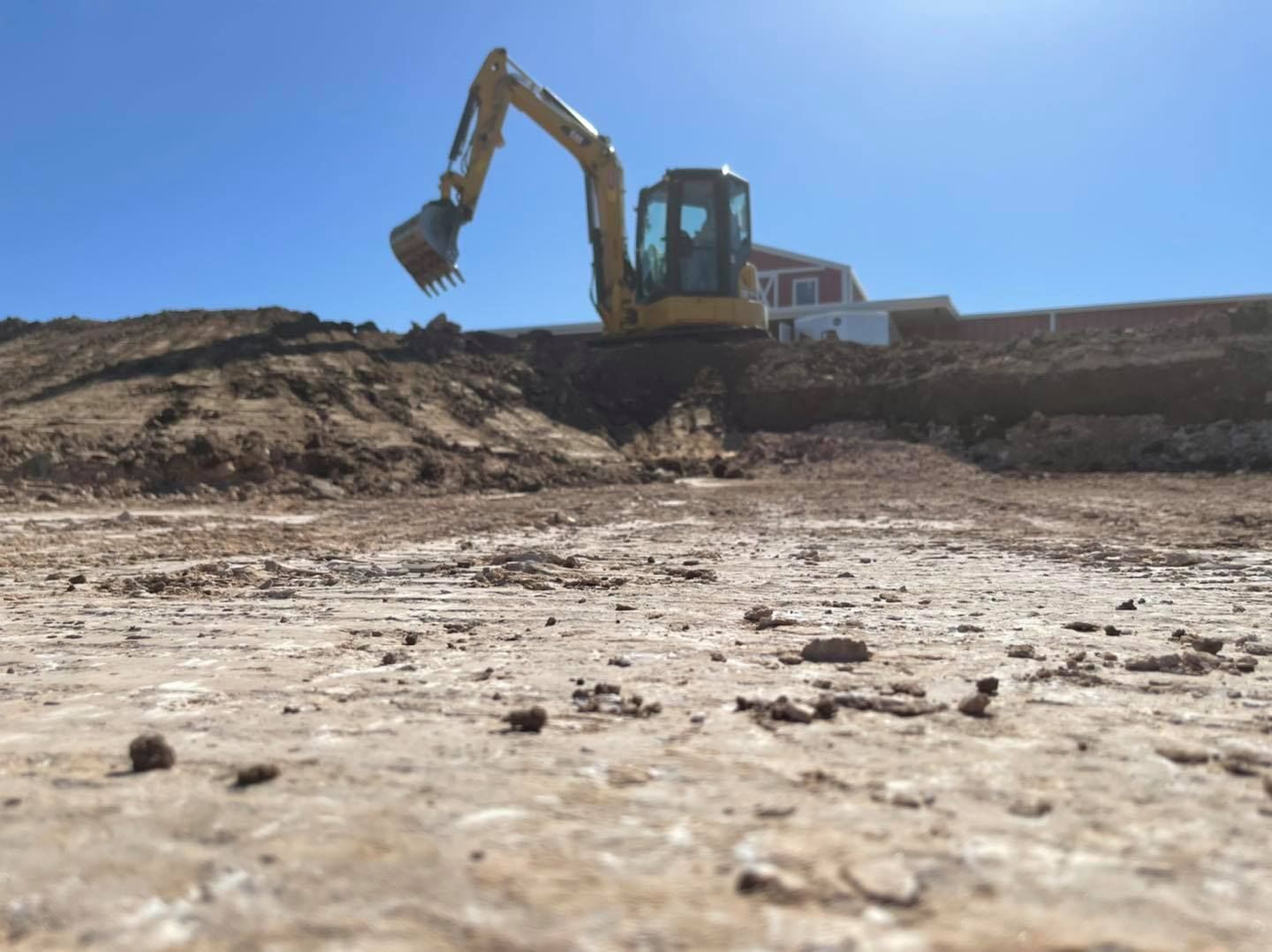 An excavator on a construction site against a bright blue sky, digging into a pile of dirt.
