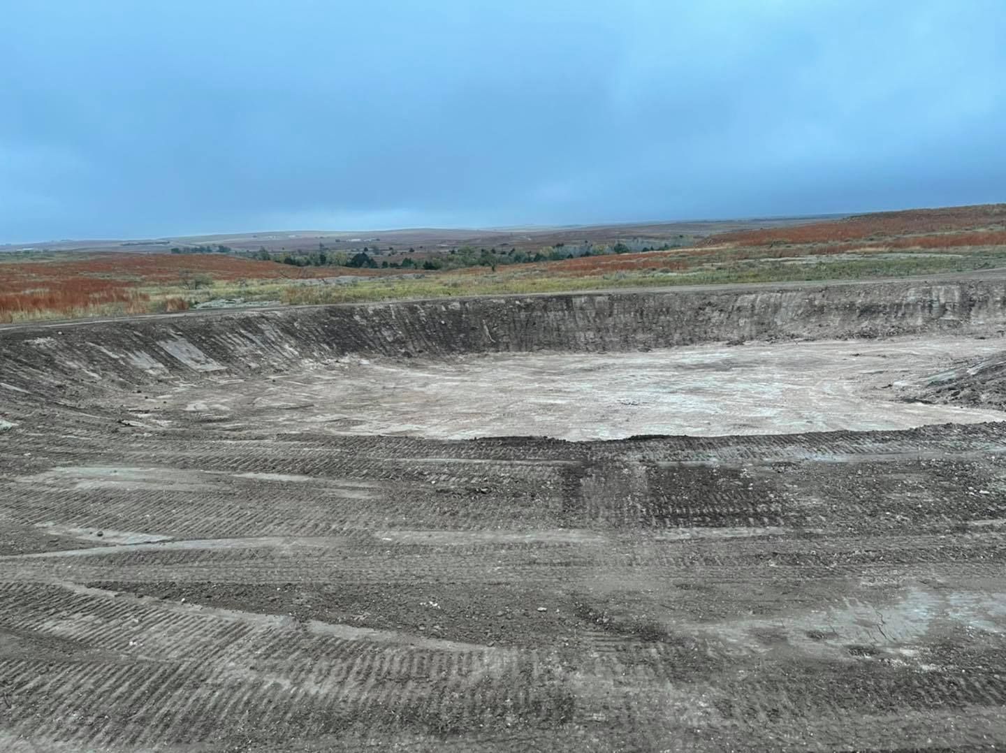 Large excavated area in a brown, barren landscape under an overcast sky.