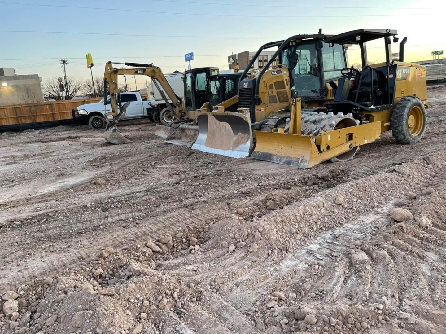 Construction site with heavy machinery: bulldozer, excavator, and truck on dirt ground.