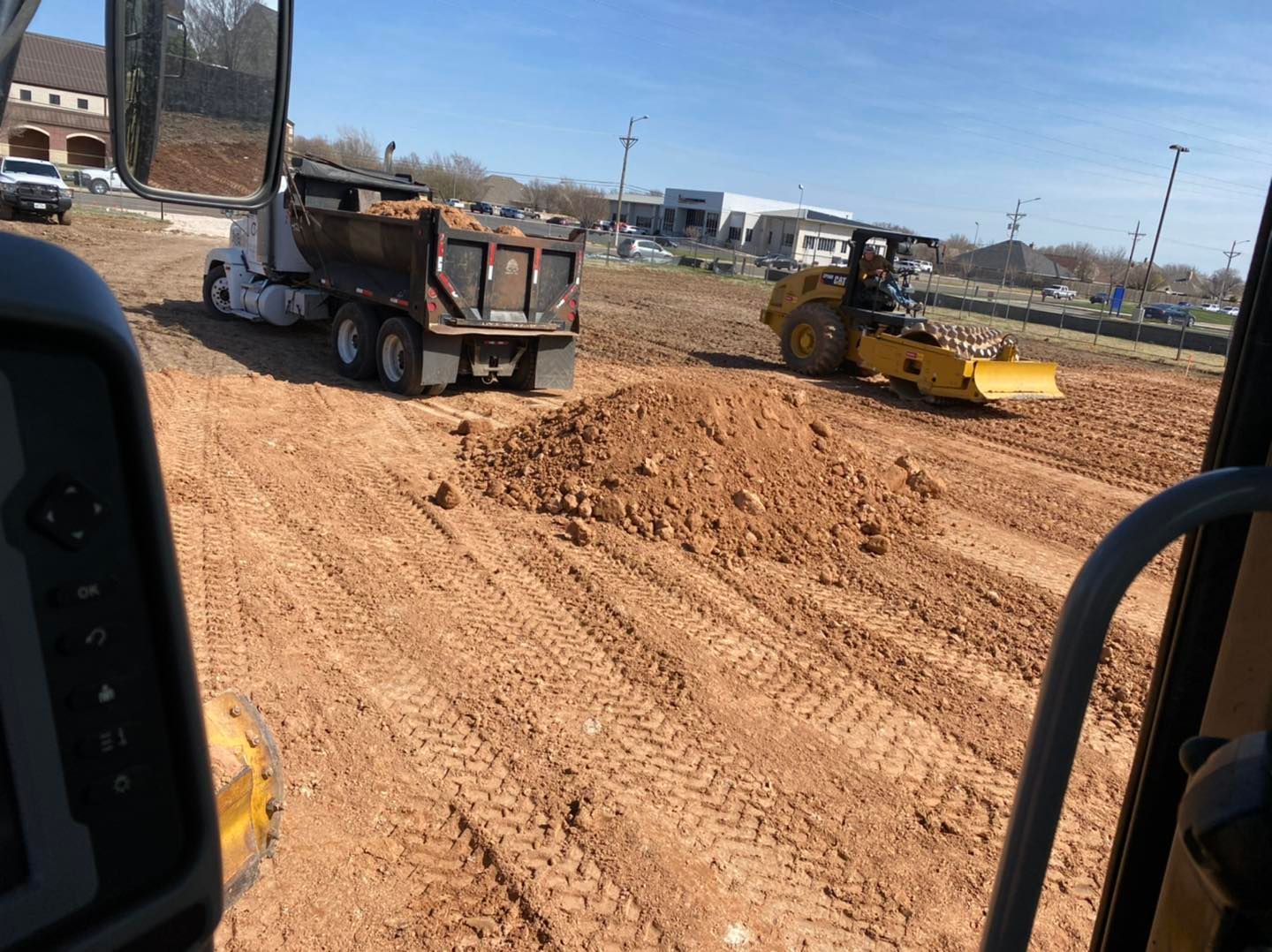 Construction site: Dump truck, yellow bulldozer grading dirt; sunny day.