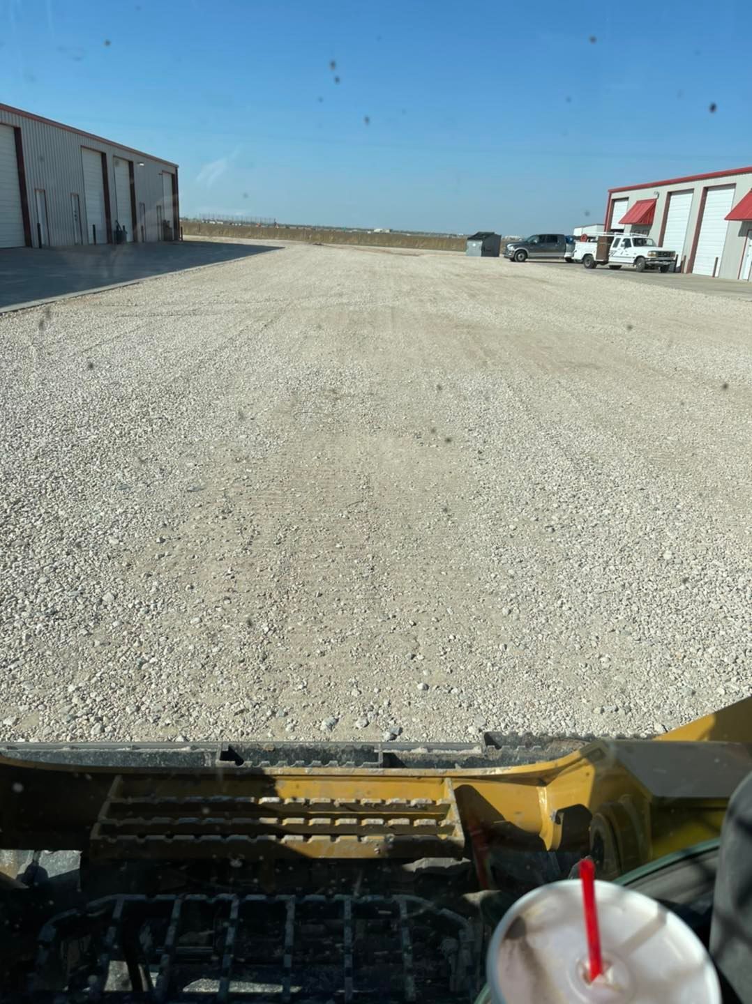 View from a tractor cab of a gravel parking lot with storage buildings under a clear sky.