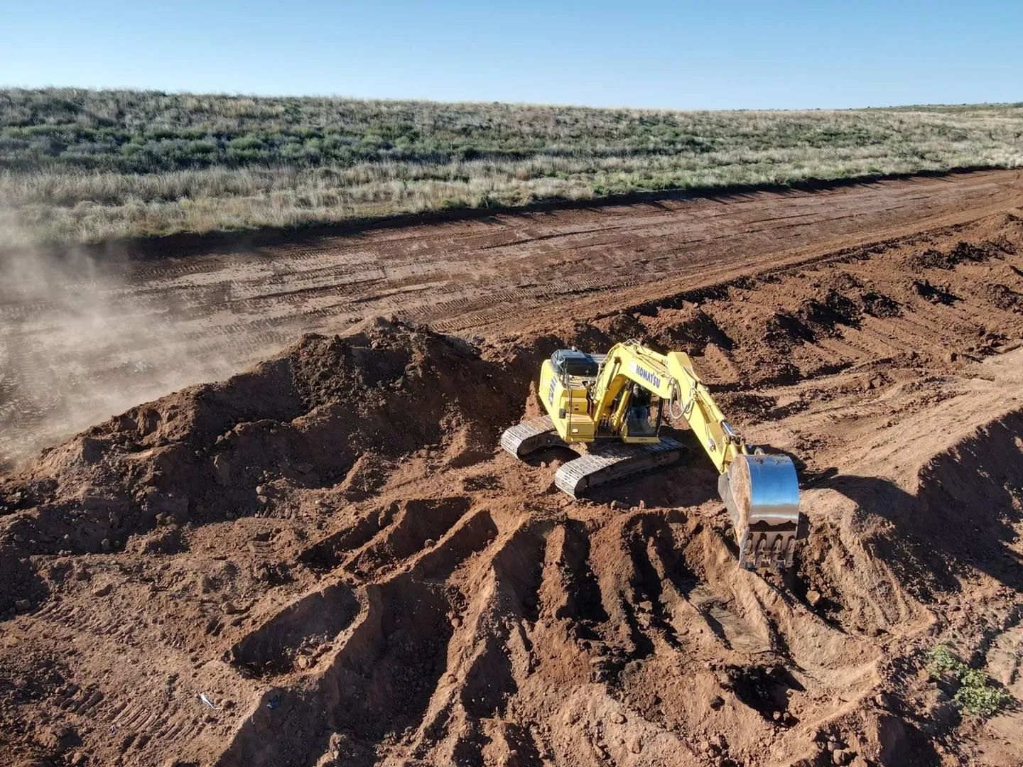 Yellow excavator digging dirt on a brown construction site under a blue sky.