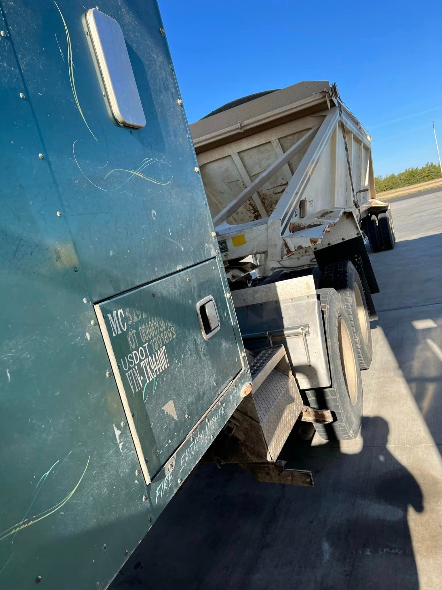 Green dump truck with the truck bed tilted up, side view.