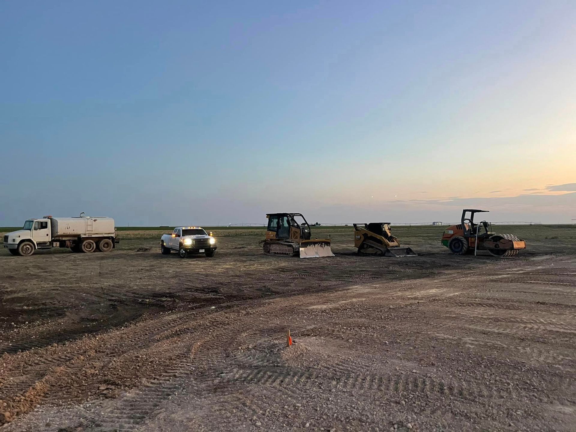 Construction vehicles parked on a dirt field at dusk.