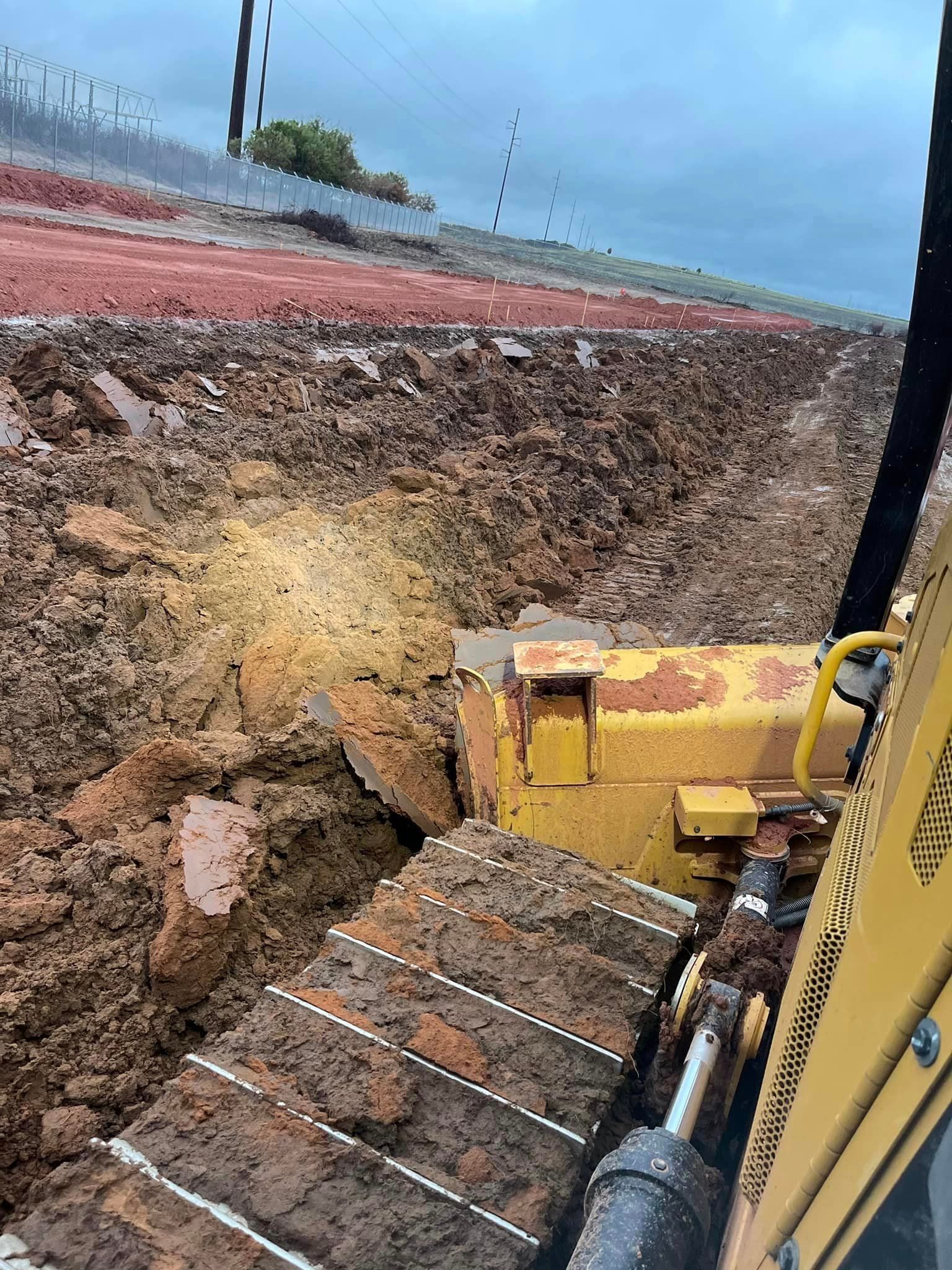 A yellow bulldozer plowing through wet, muddy earth next to a red and white embankment.