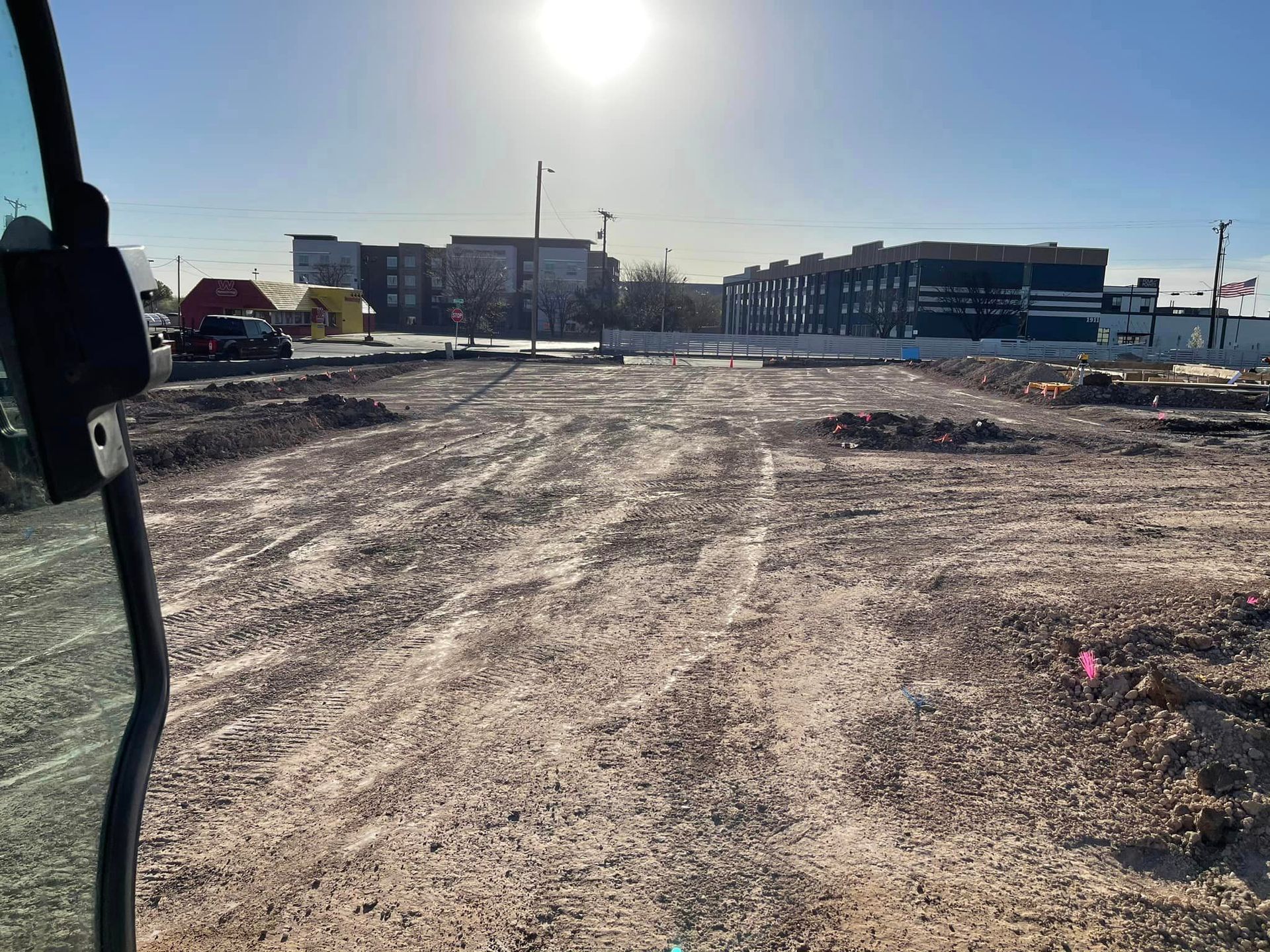 Construction site with gravel ground, buildings in background, sunny day.