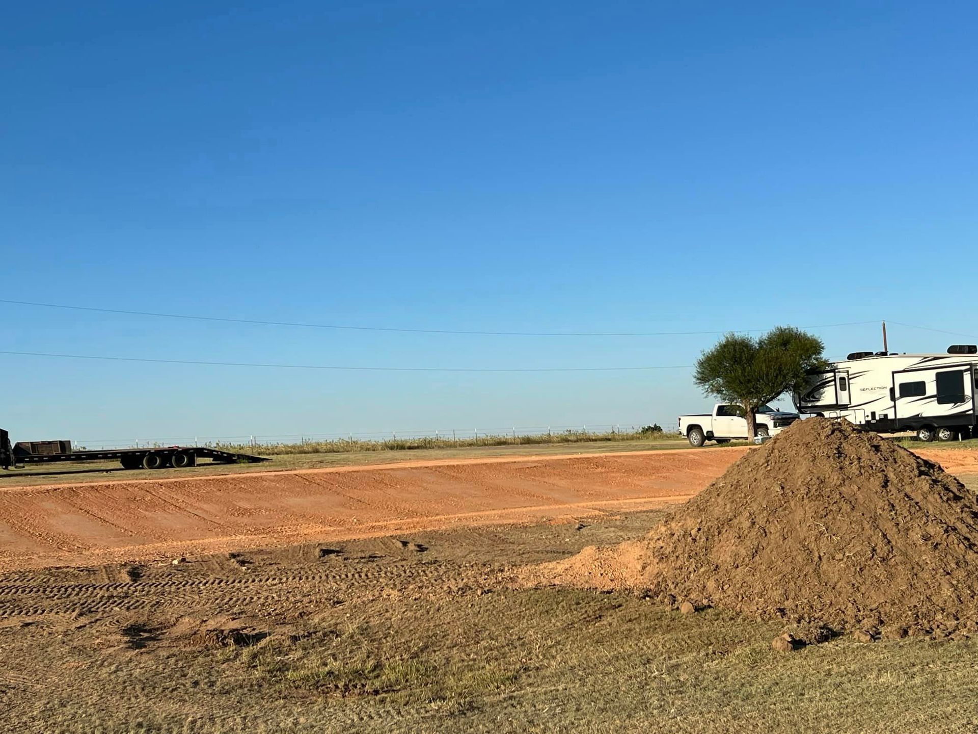 Construction site with dirt mounds and trucks against a clear blue sky.