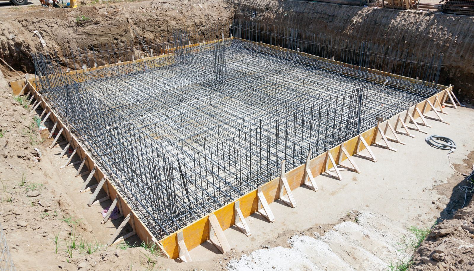 Construction site with a square foundation formwork containing rebar, ready for concrete pouring.