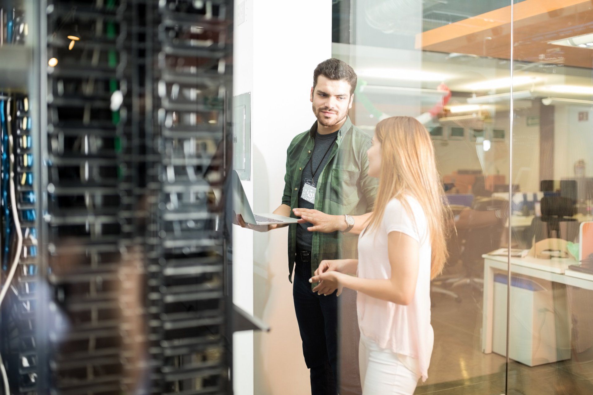 A man and a woman are standing next to each other in a server room.