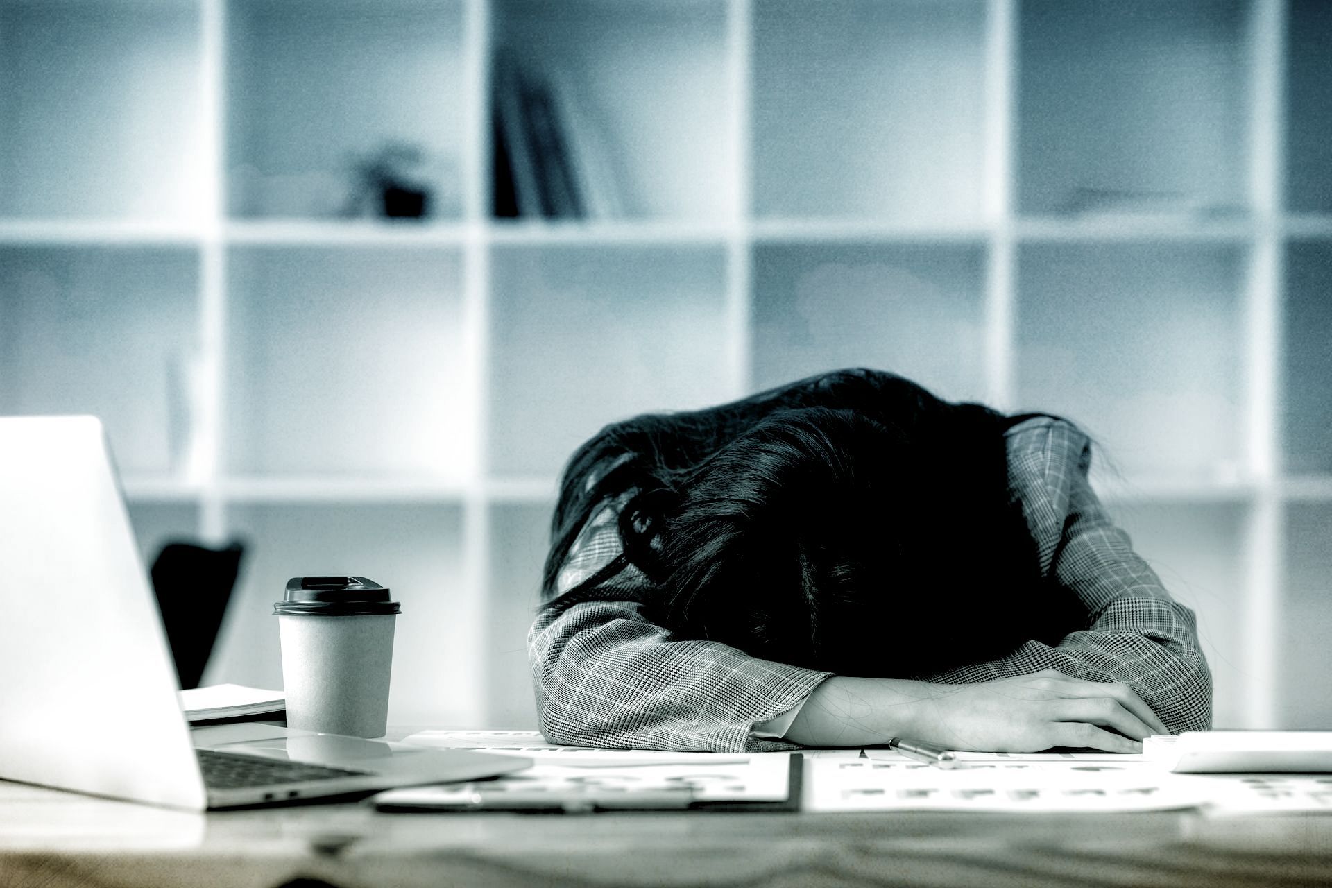 a woman is sleeping at a desk in front of a laptop computer .