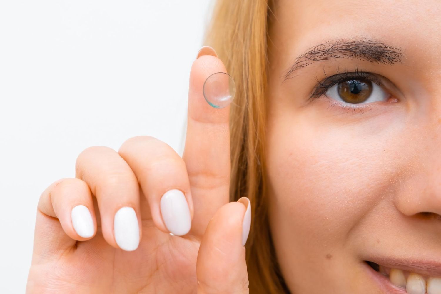 A woman is holding a contact lens on her finger.