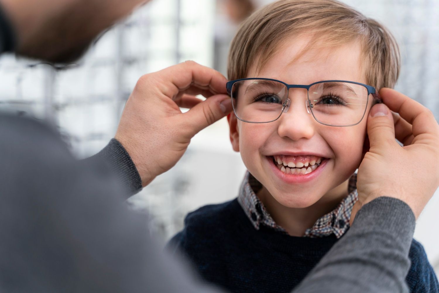 A child smiles while an adult adjusts his new eyeglasses in an optical shop.