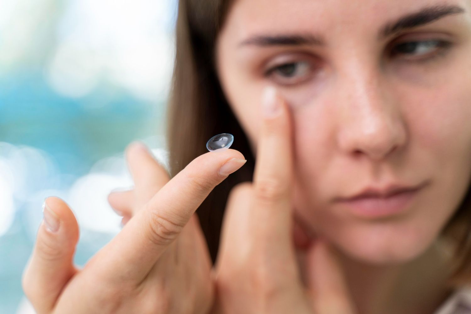 Woman inserts a contact lens into her eye; close-up shows lens on fingertip and focused face.