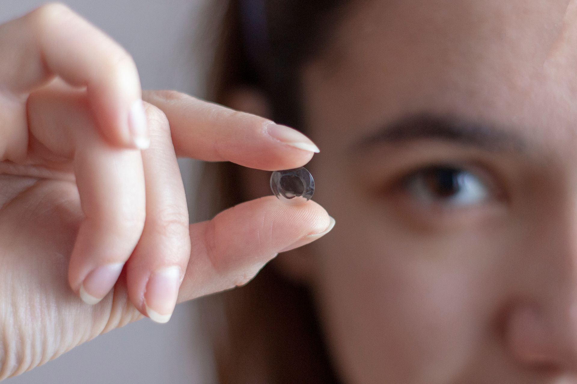 A woman is holding a contact lens in her hand.