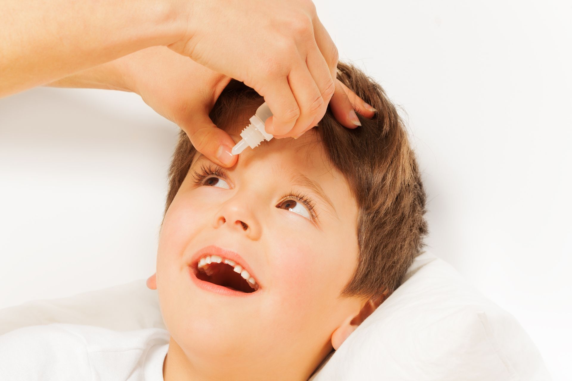 A person is applying eye drops to a young boy 's eye.