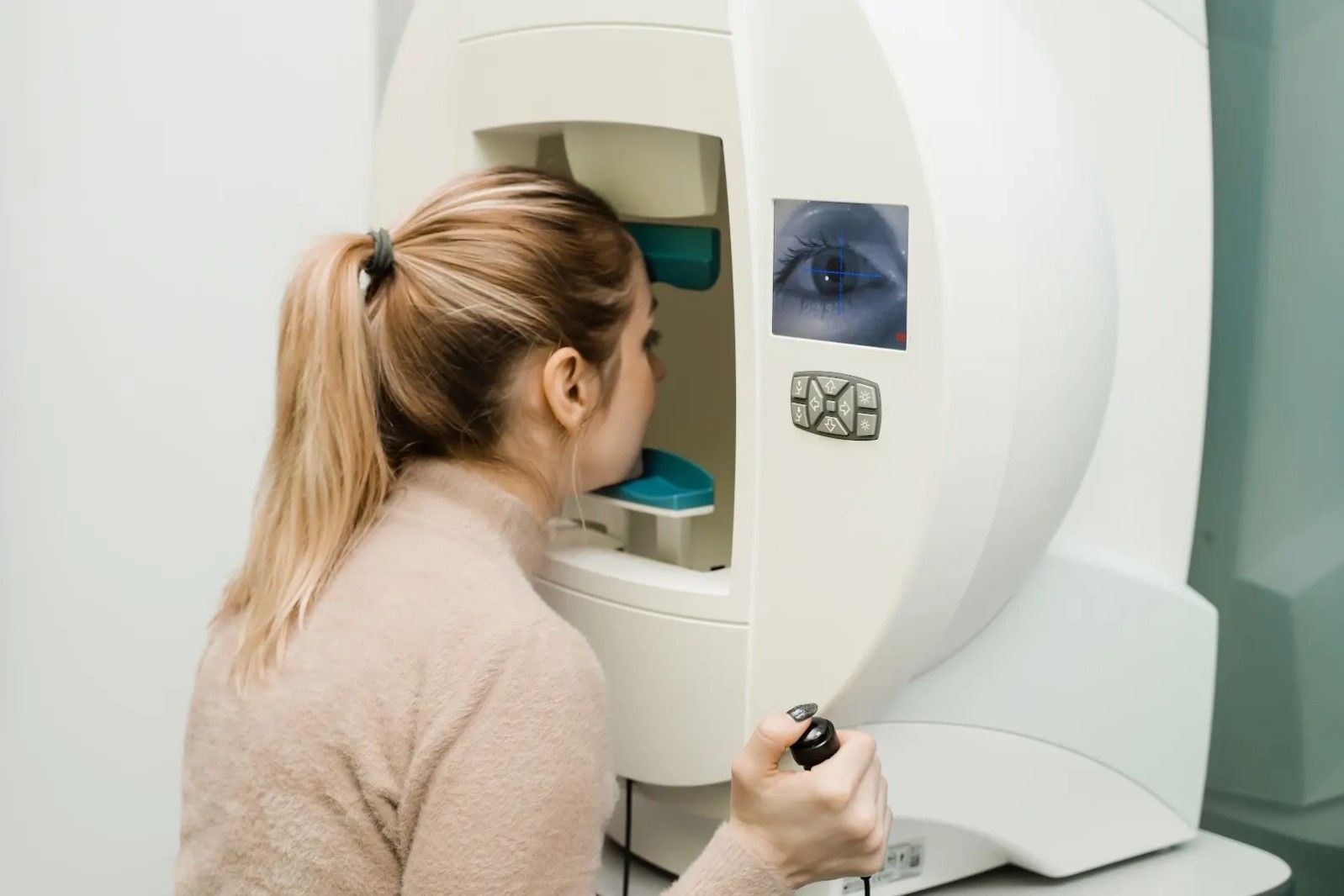 Woman undergoing eye exam using a white machine; screen displays an eye image.