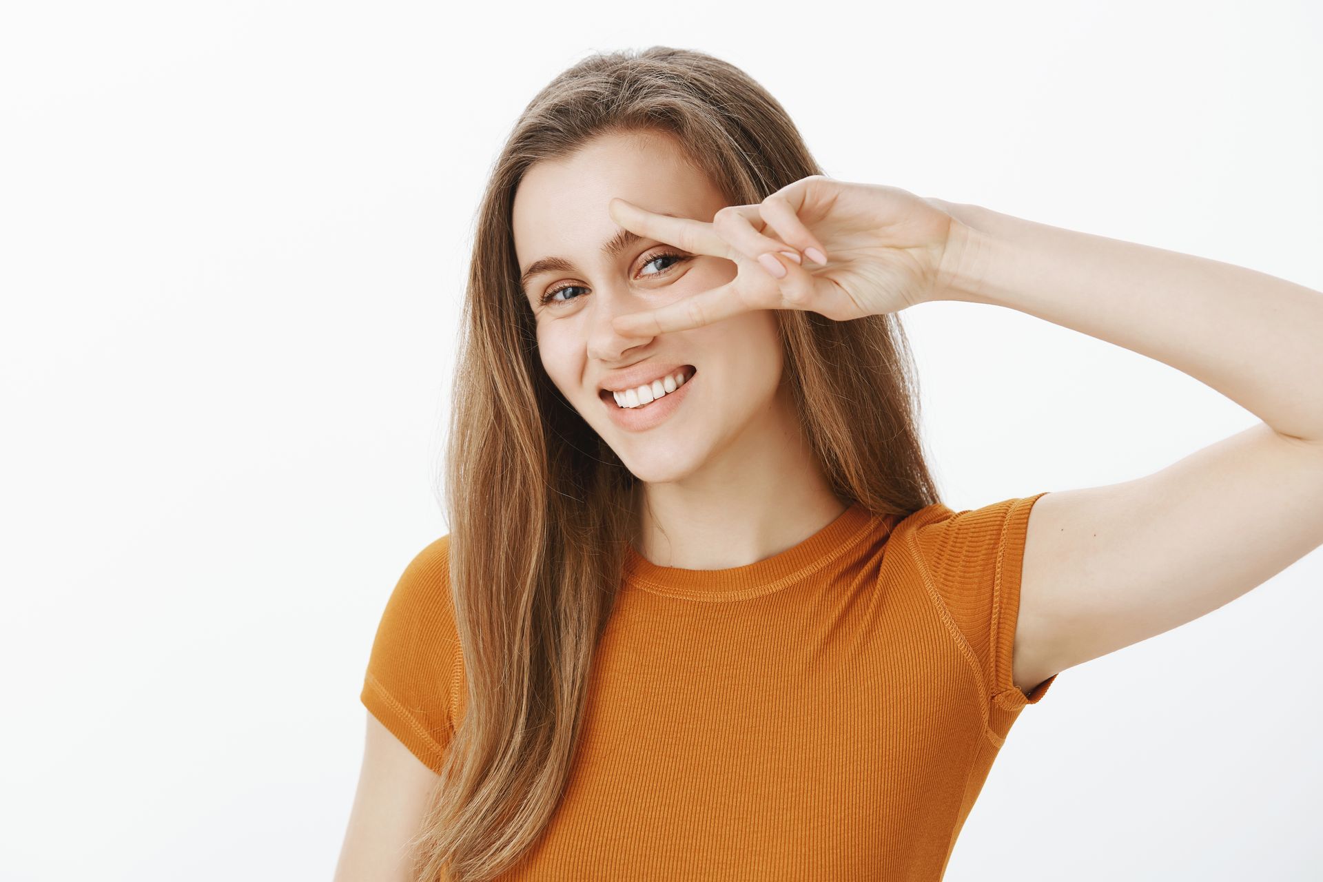 A young woman is smiling and making a peace sign with her hand.