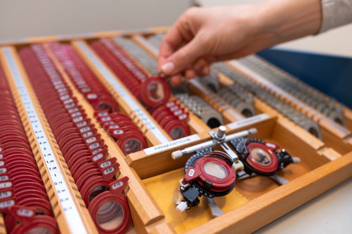A person is holding a pair of red lenses in a wooden tray.