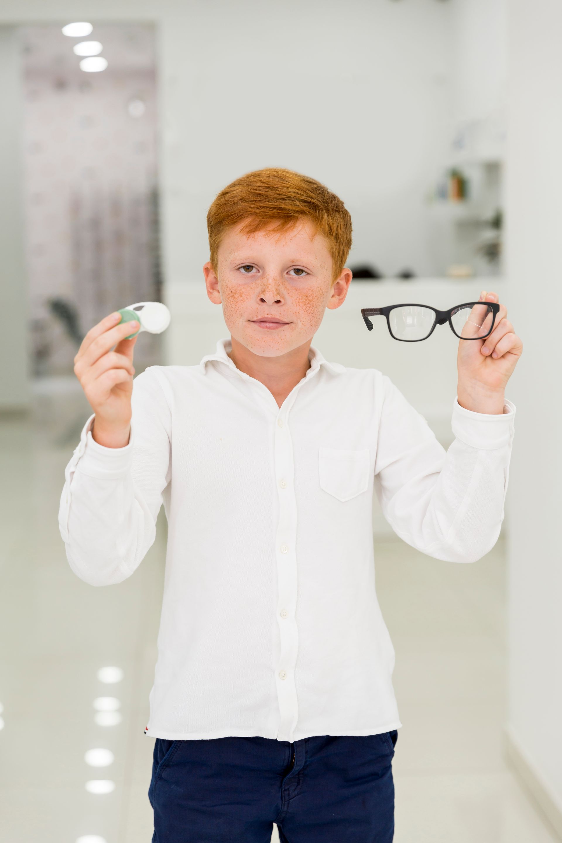 A young boy is holding a pair of glasses and a contact lens.