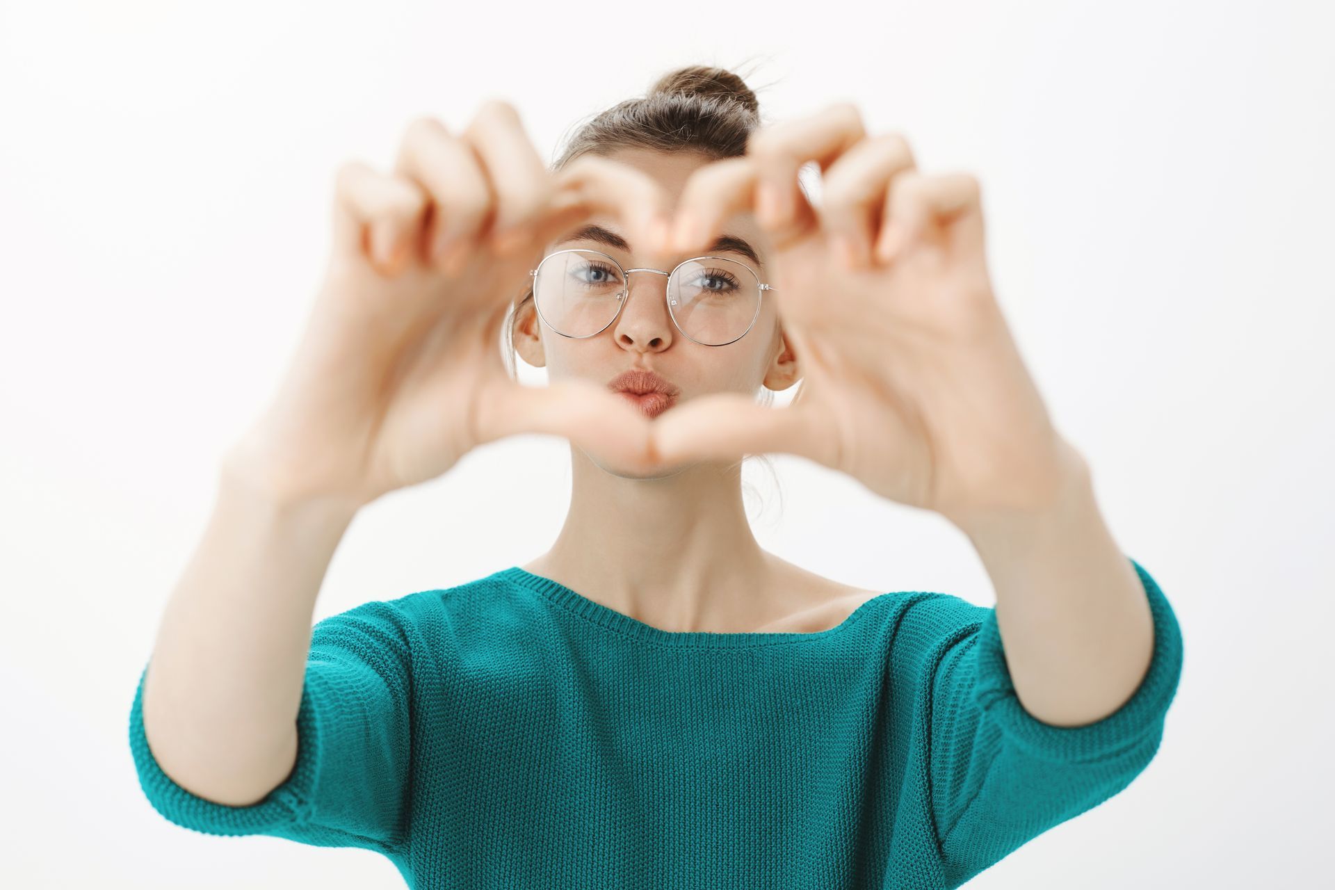 A woman wearing glasses is making a heart shape with her hands.