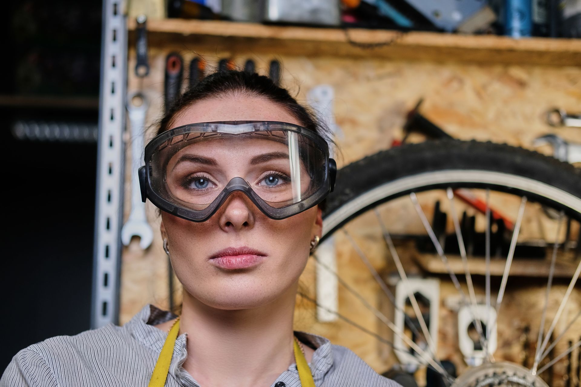 A woman wearing safety goggles is standing in front of a bicycle wheel.