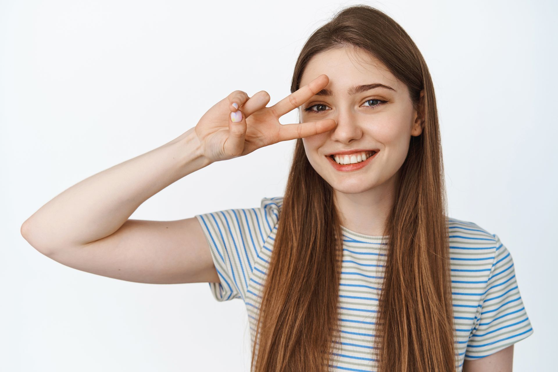 A young woman is smiling and making a peace sign with her hand.