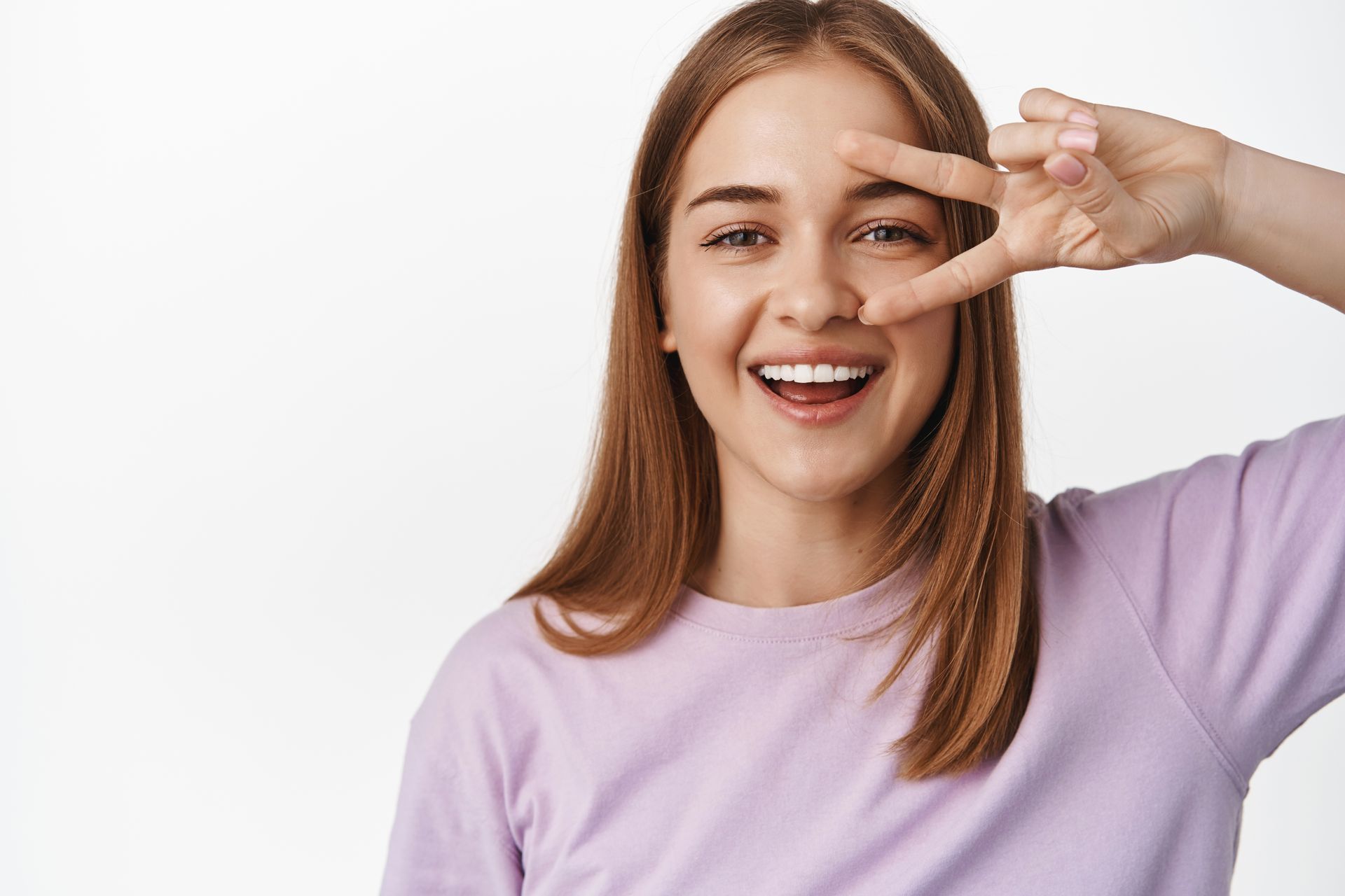 A young woman is smiling and making a peace sign with her hand.