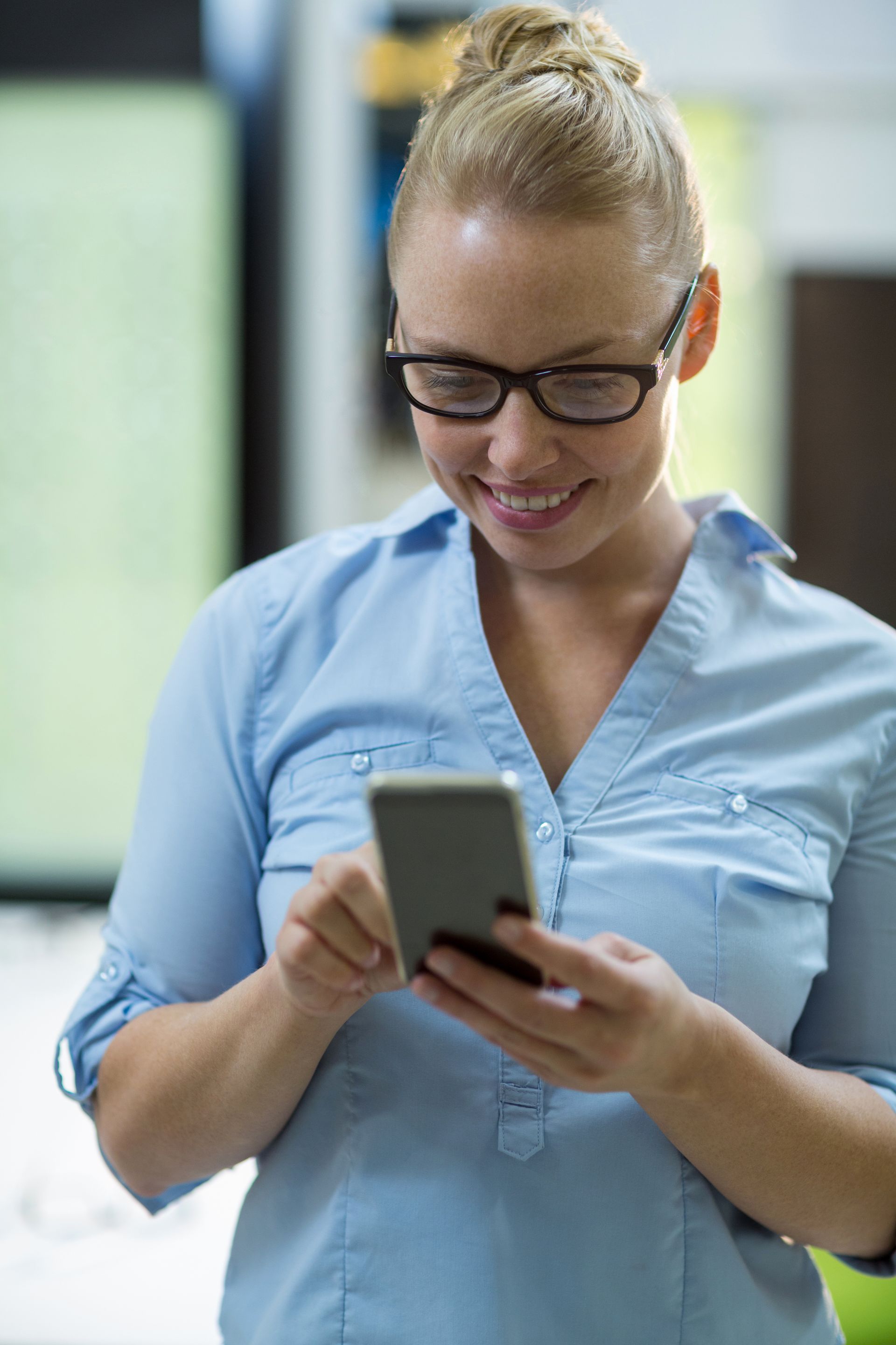 A woman wearing glasses is looking at her cell phone.