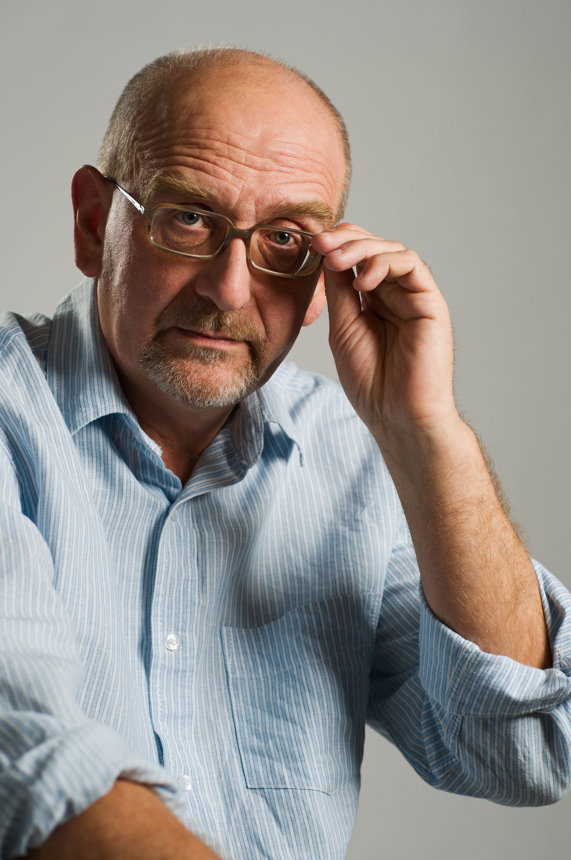 A man with glasses and a beard is adjusting his glasses.