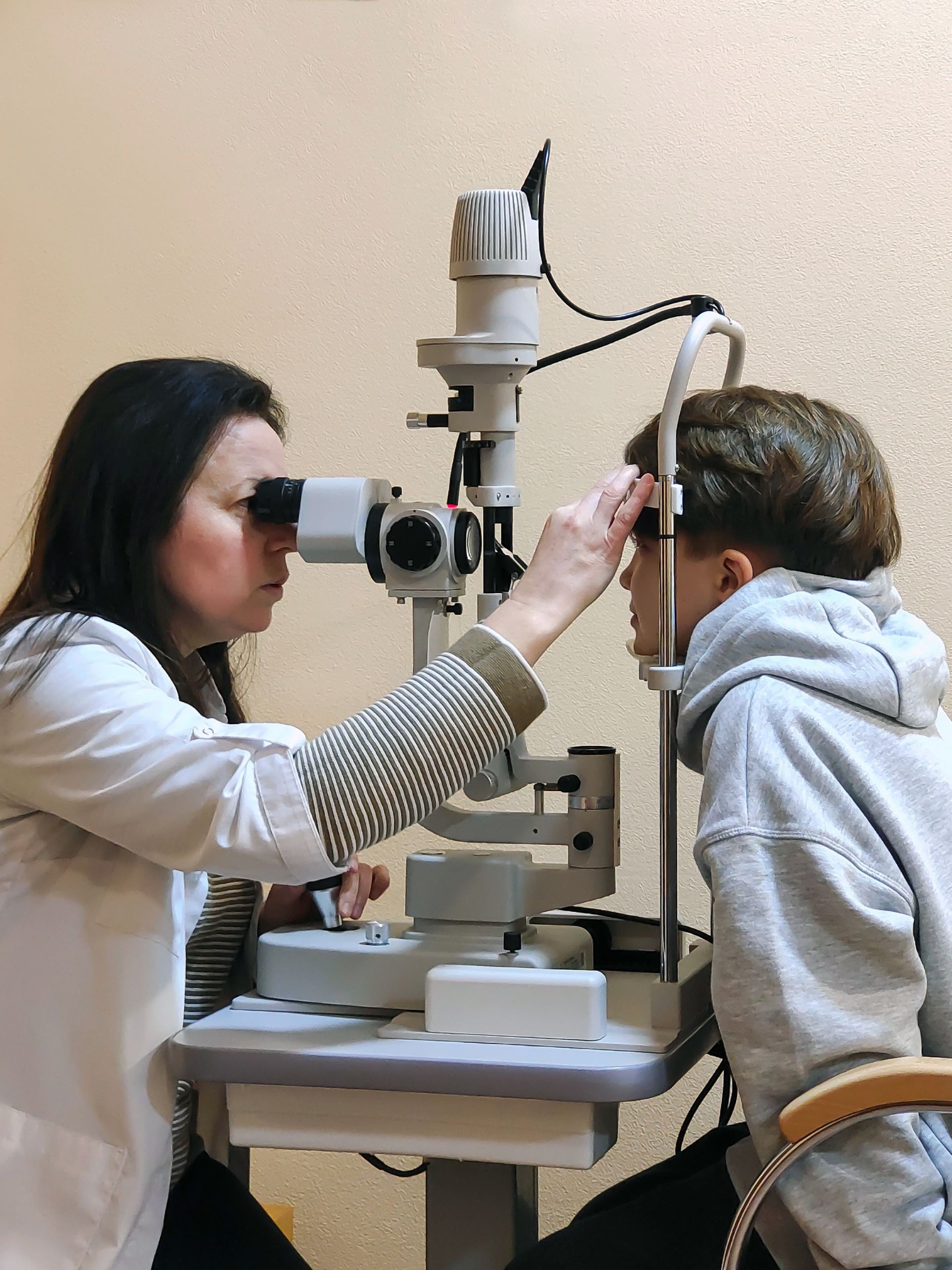 A woman is examining a boy 's eye with a microscope.