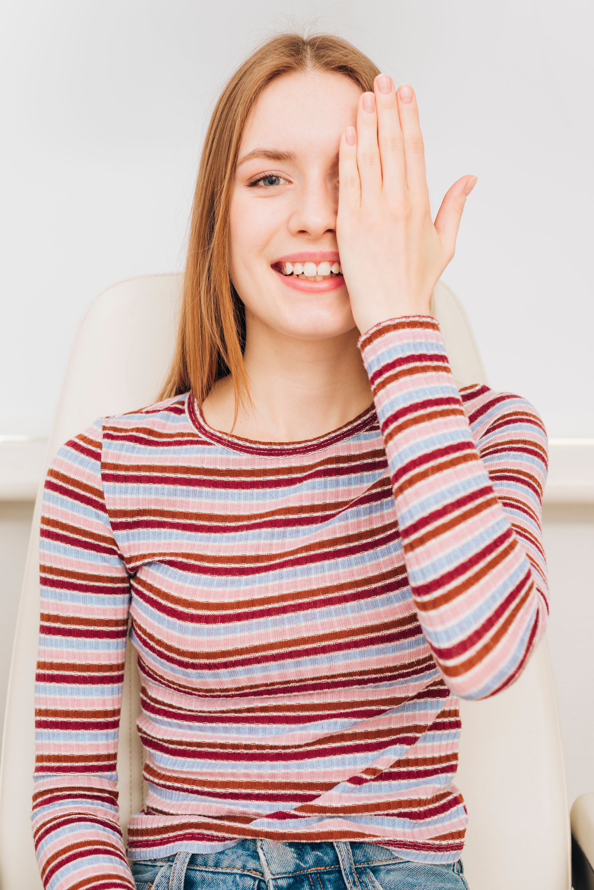 A woman in a striped shirt is covering her eye with her hand.