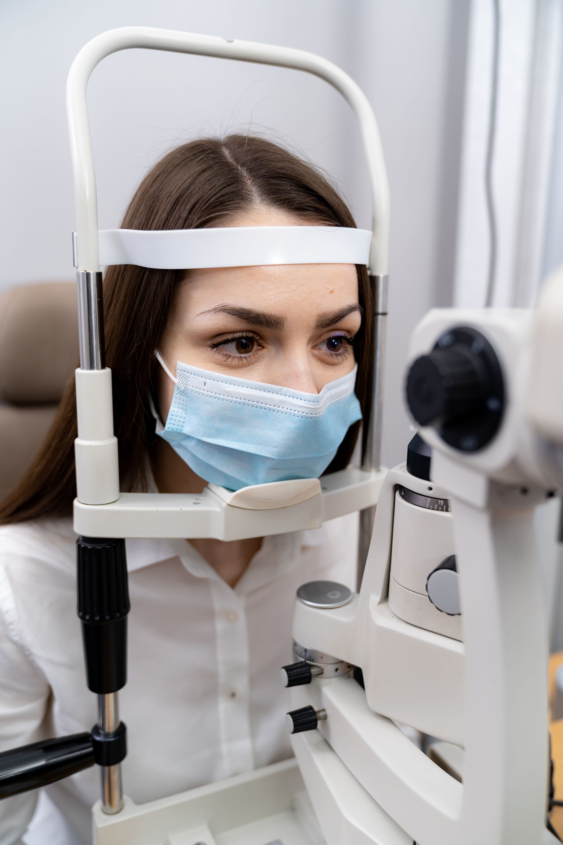 A woman wearing a mask is getting her eyes examined by an ophthalmologist.