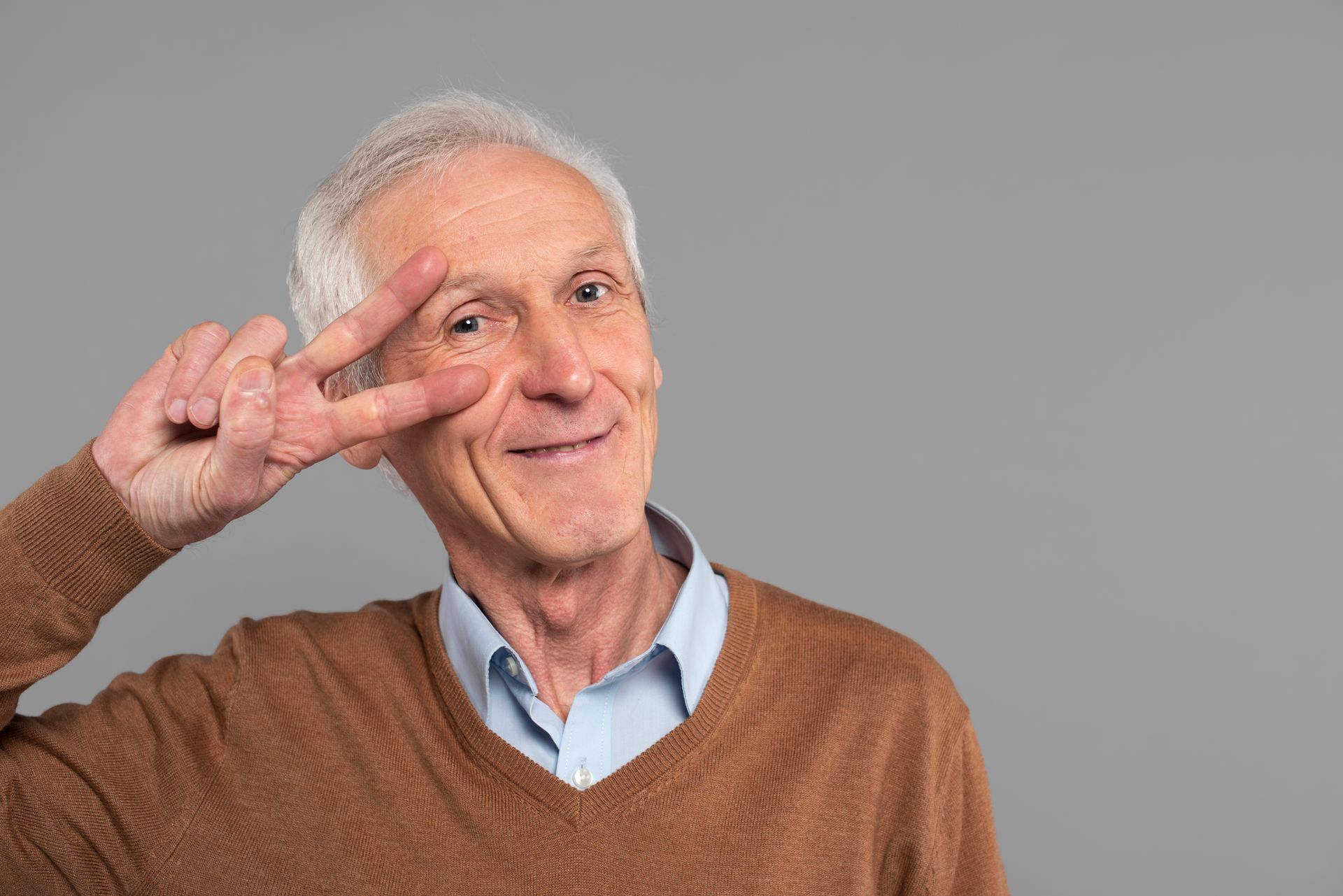 An elderly man is making a peace sign with his hands.