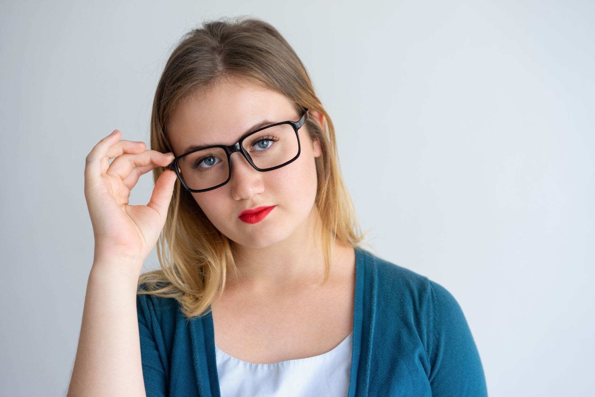 A woman wearing glasses and a blue sweater is adjusting her glasses.