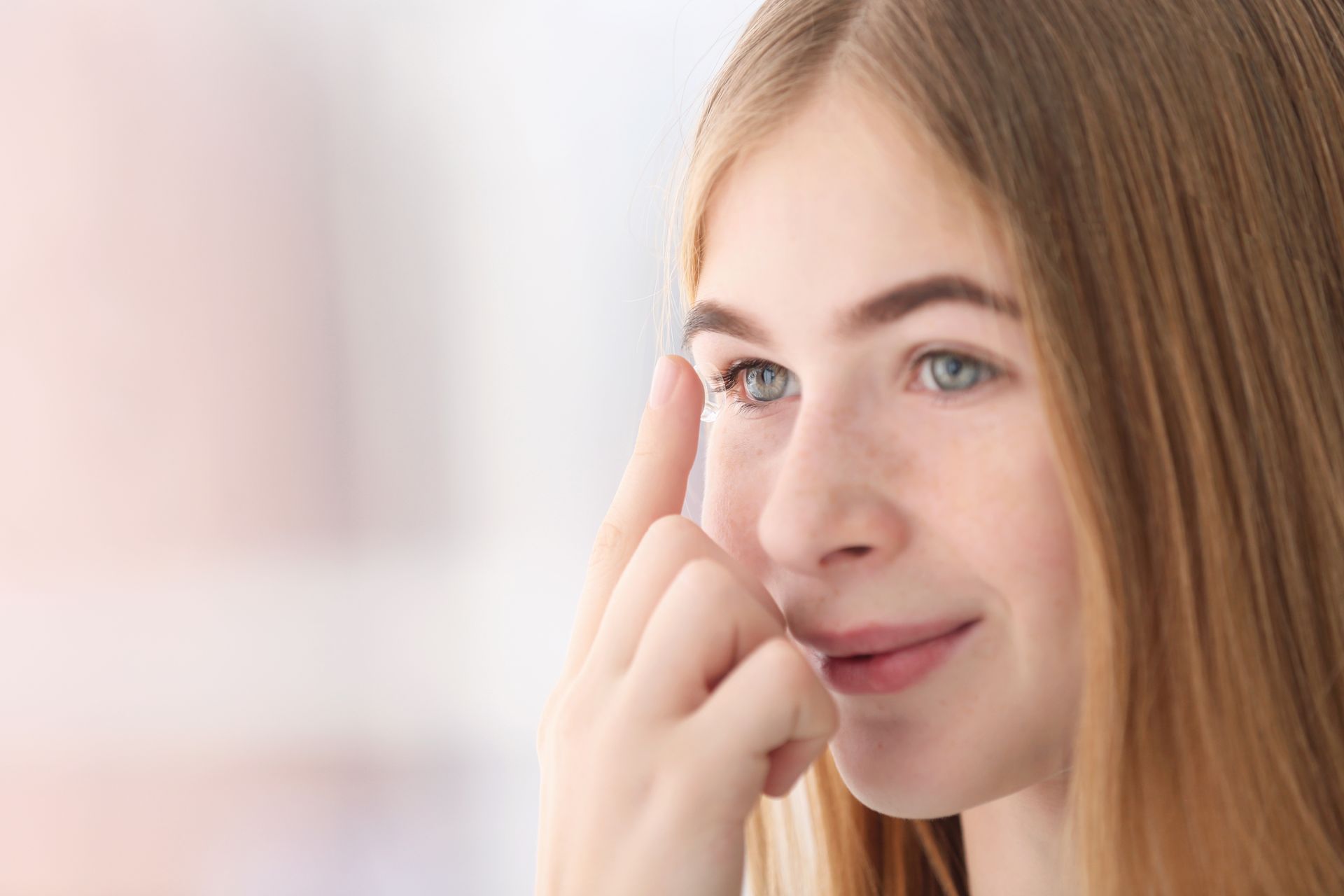 A young woman is putting a contact lens in her eye.