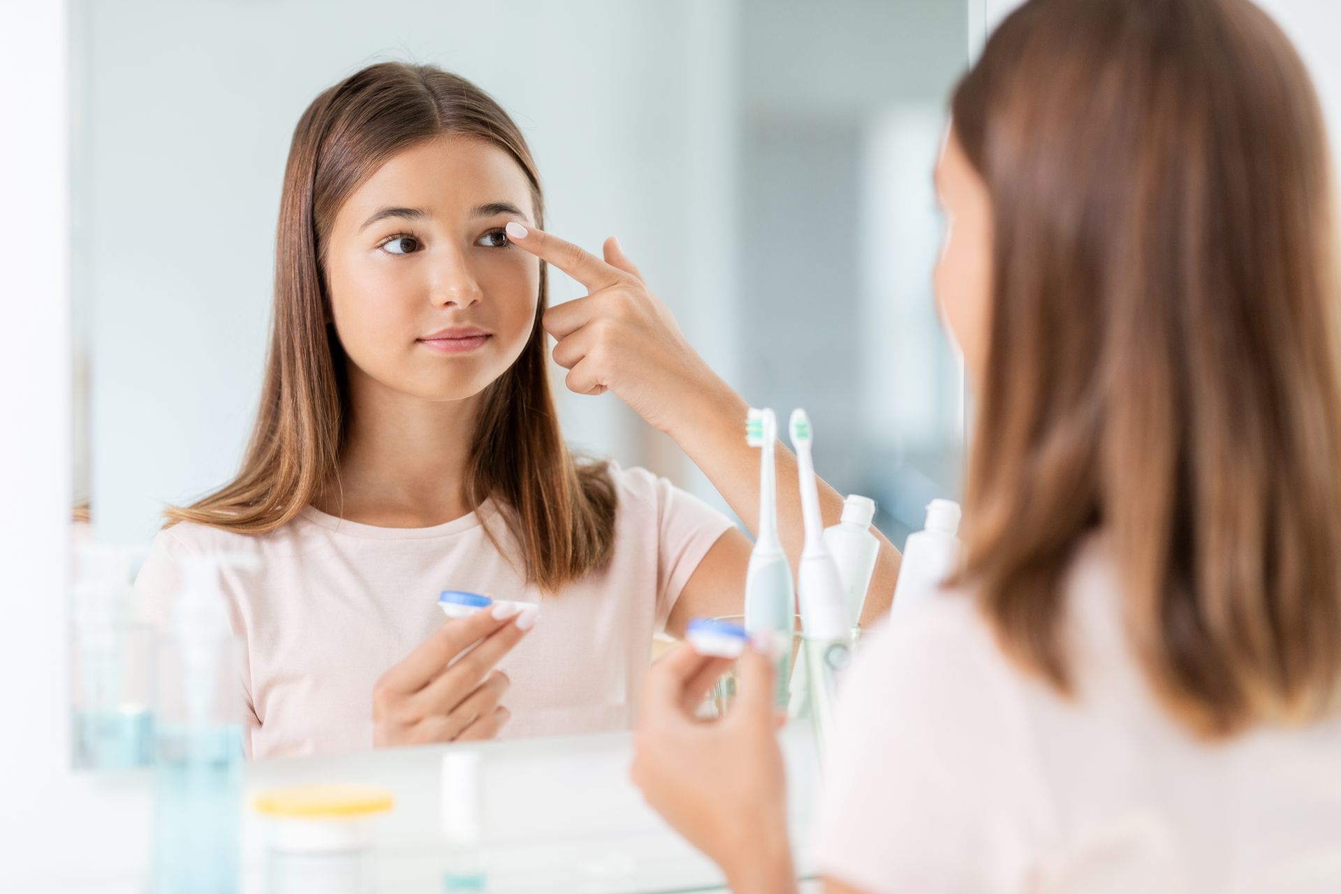 A woman is applying contact lenses to her eye in front of a mirror.