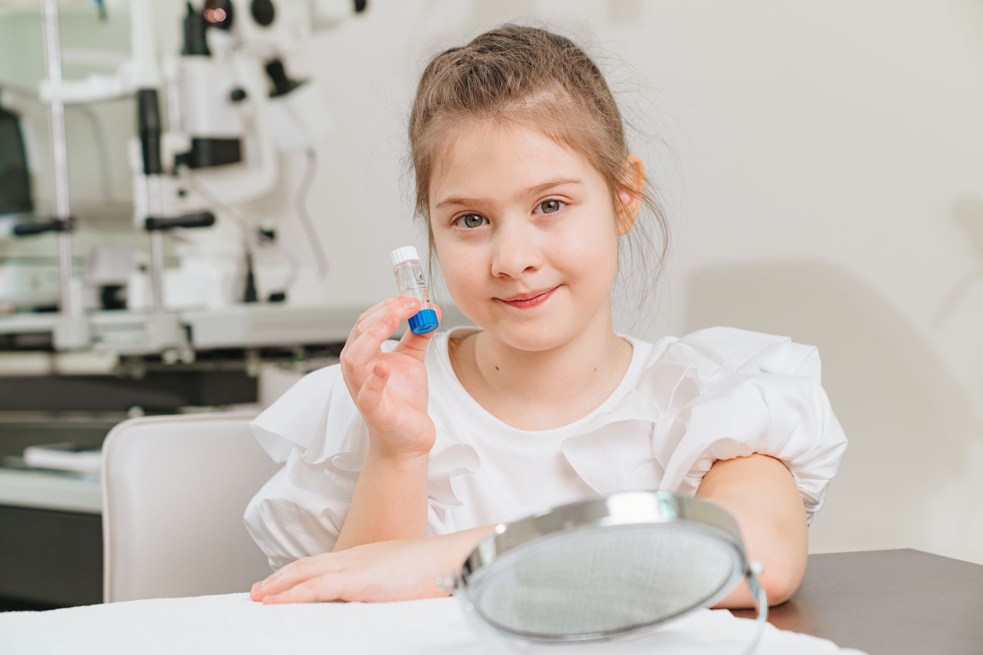 A little girl is holding a contact lens in front of a mirror.