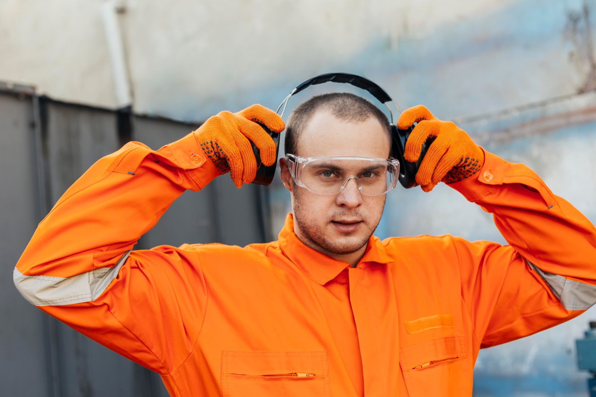 A man in an orange uniform is wearing headphones and safety goggles.