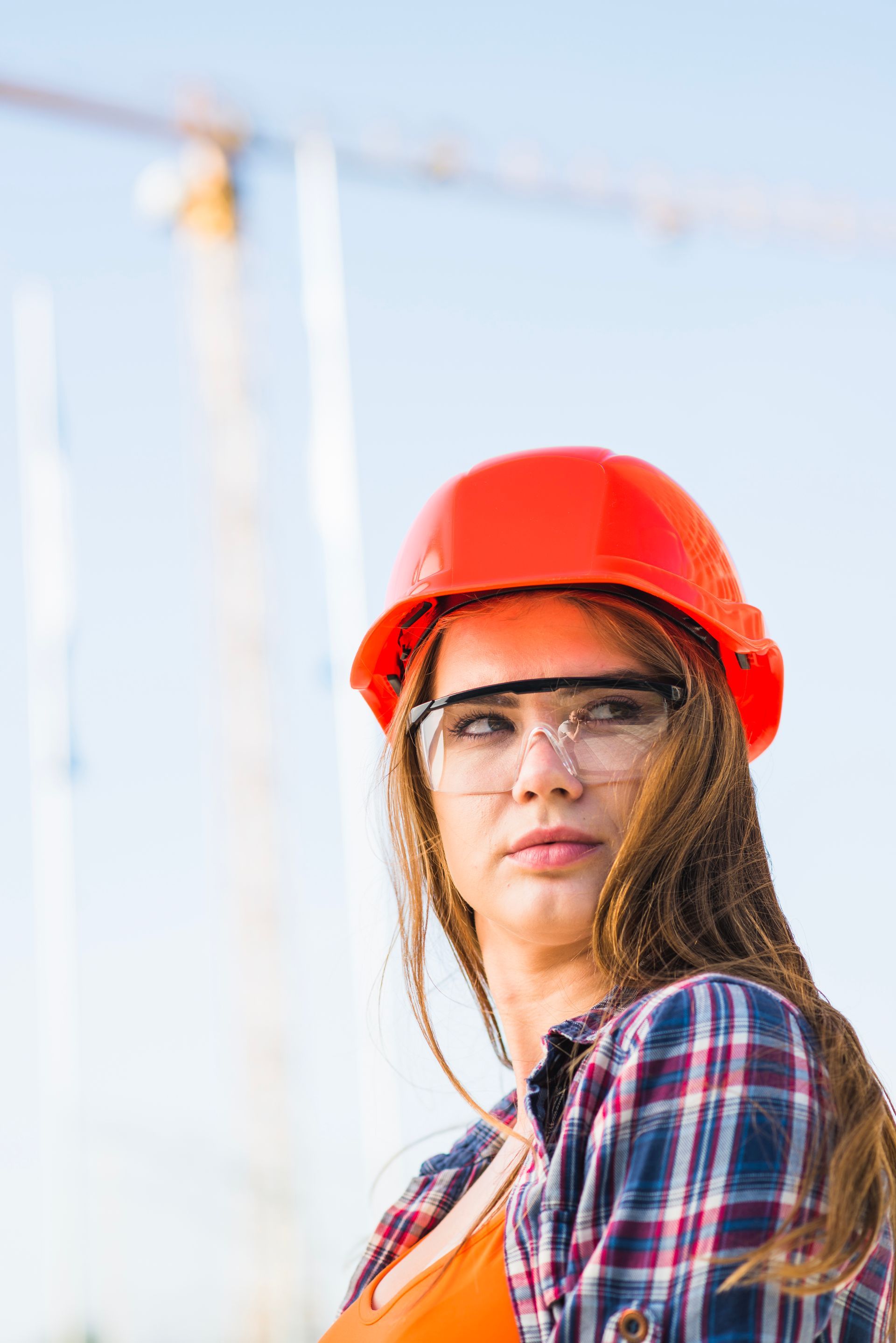 A woman wearing a hard hat and safety glasses is standing in front of a construction site.