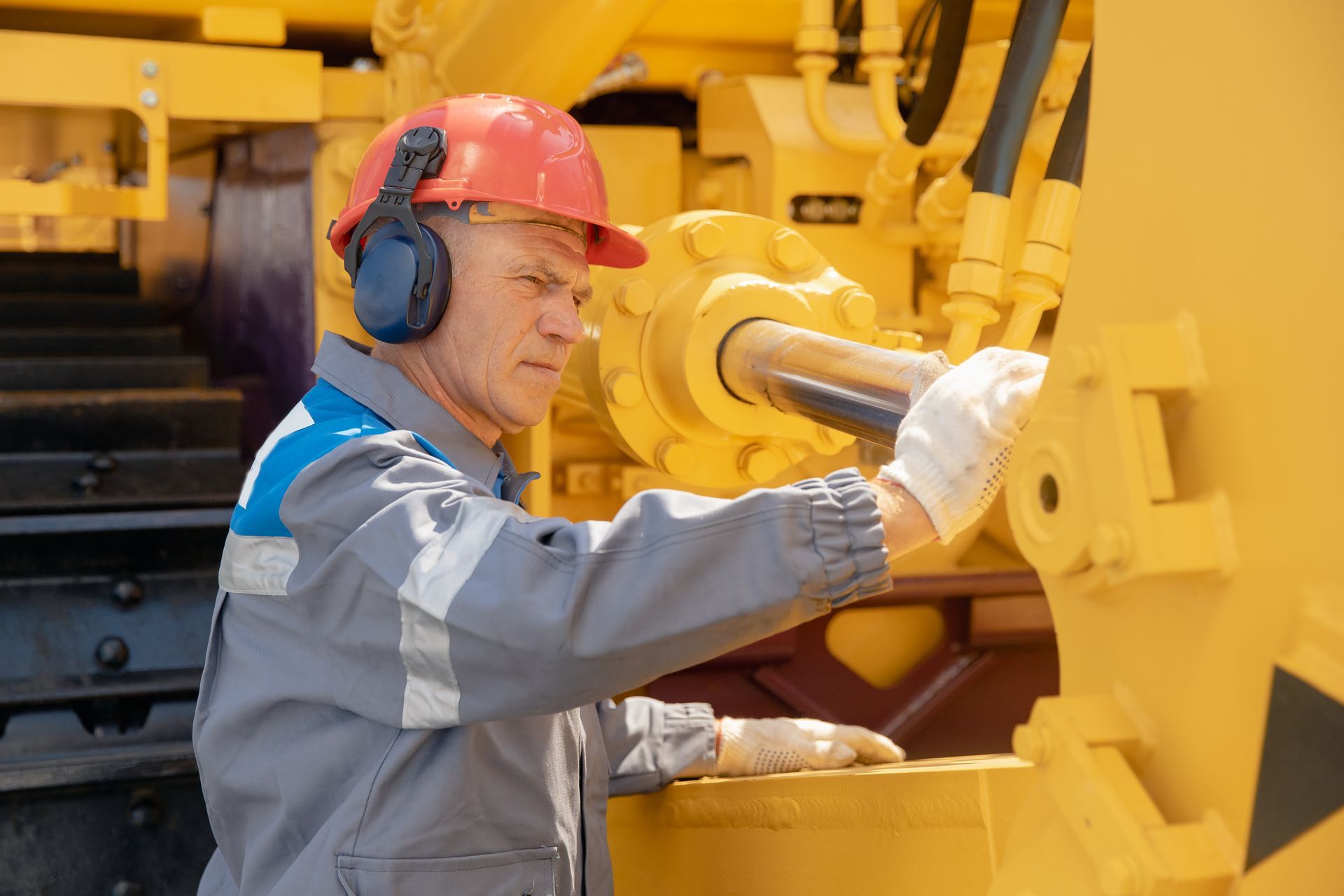 Worker inspecting heavy machinery hydraulics while wearing protective gear. Worker inspecting heavy machinery hydraulics while wearing protective gear.
