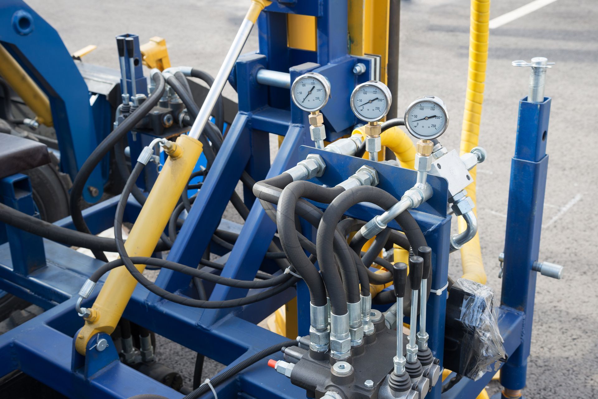 Close-up of blue and yellow machinery with hydraulic lines, gauges, and cylinders, possibly for construction or agriculture.