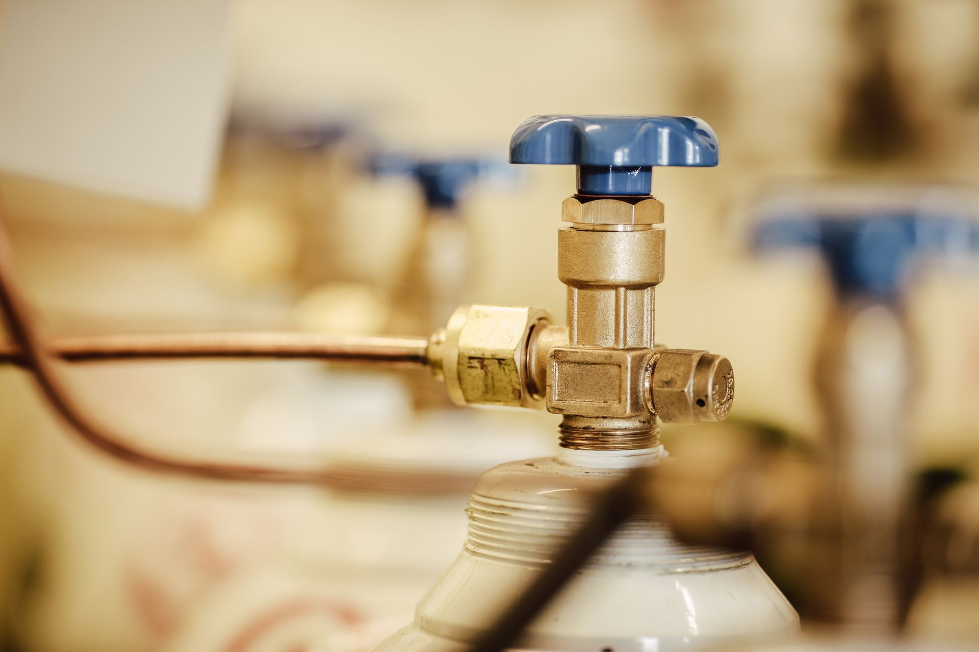 A close-up of a brass gas cylinder valve with a blue handle; a copper tube is connected to the valve.