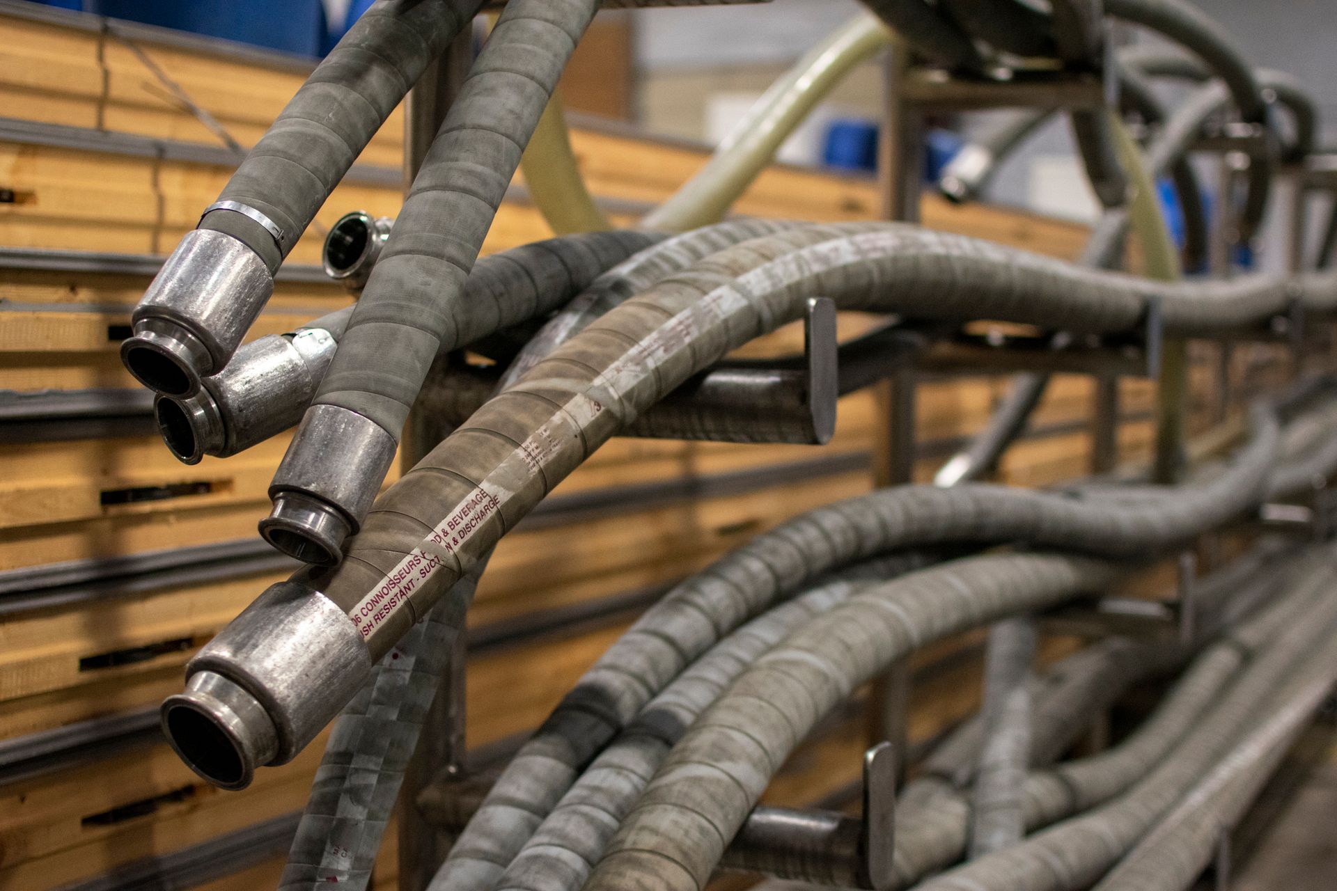 Hoses with metal connectors on a rack, likely for industrial use. They are gray and arranged in a row against a wooden background.