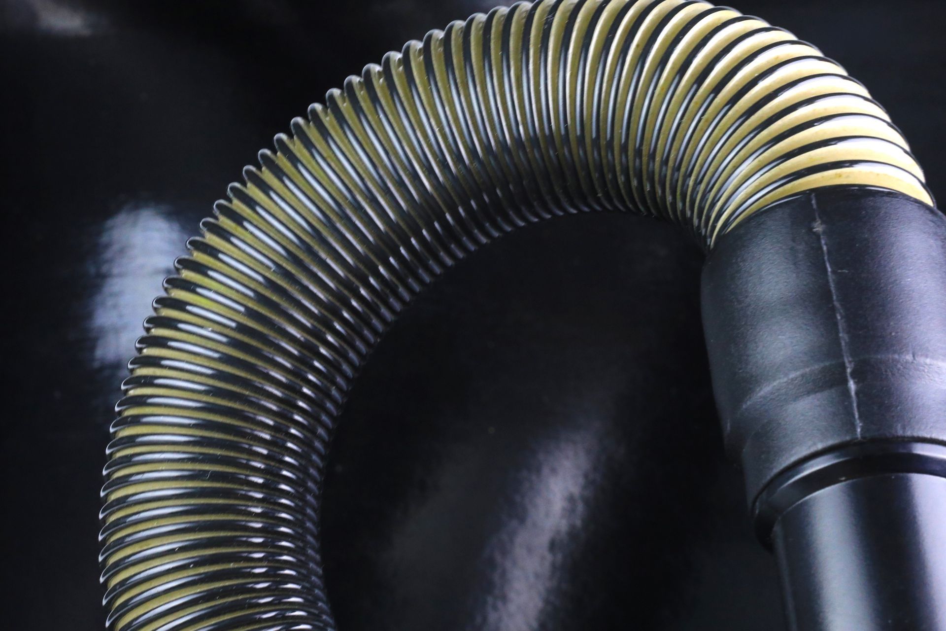 Flexible, ribbed vacuum hose curving against a black background, with a black plastic nozzle visible.