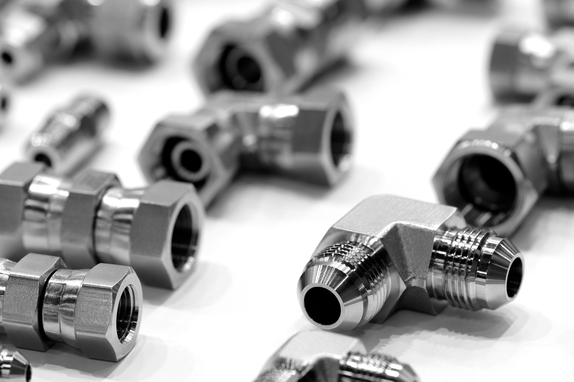 Close-up of various shiny, metallic pipe fittings, including elbows, tees, and connectors, scattered on a white surface.