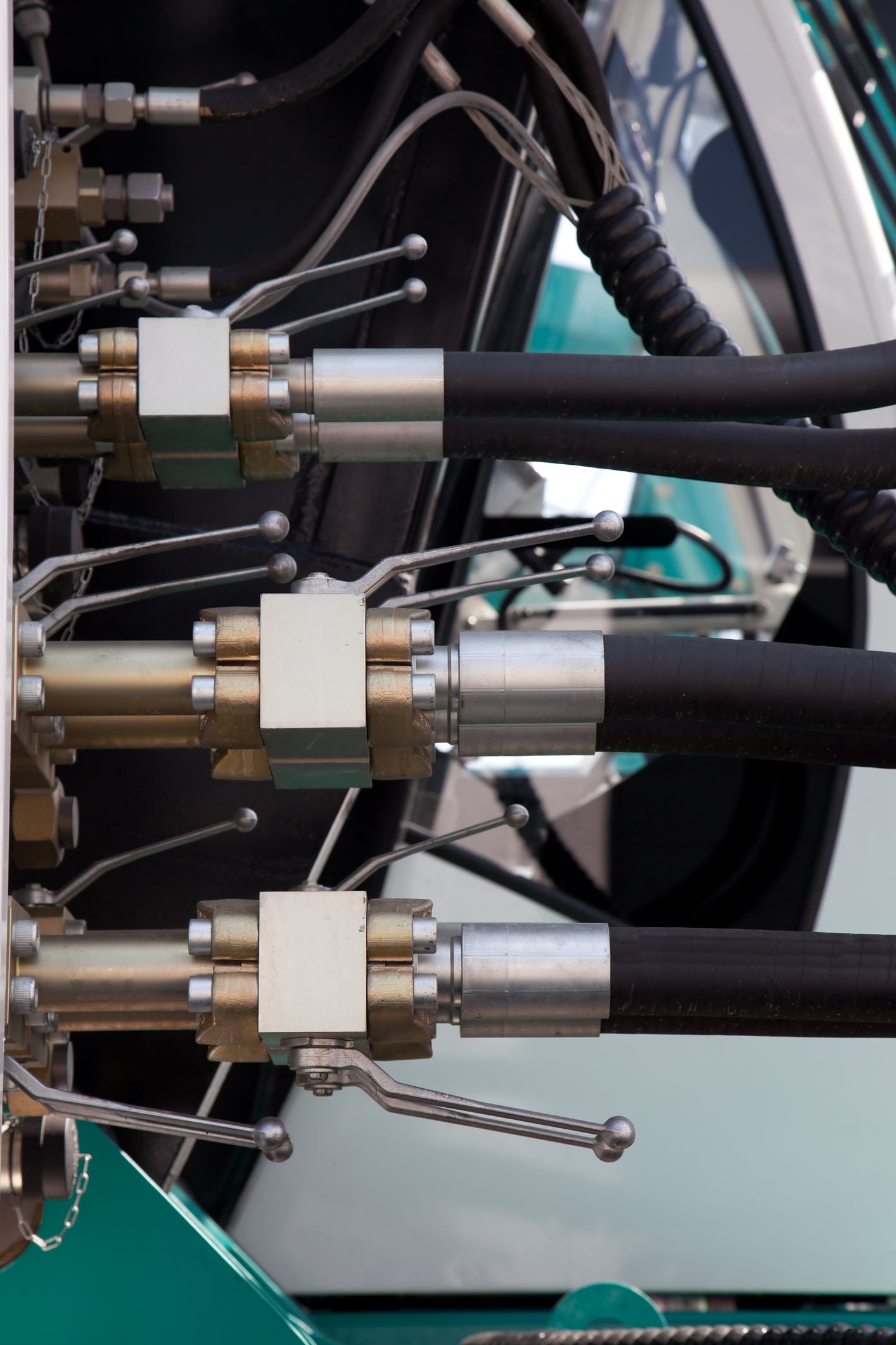 Close-up of hydraulic hoses and connectors on machinery; black hoses, silver fittings, and metal levers.