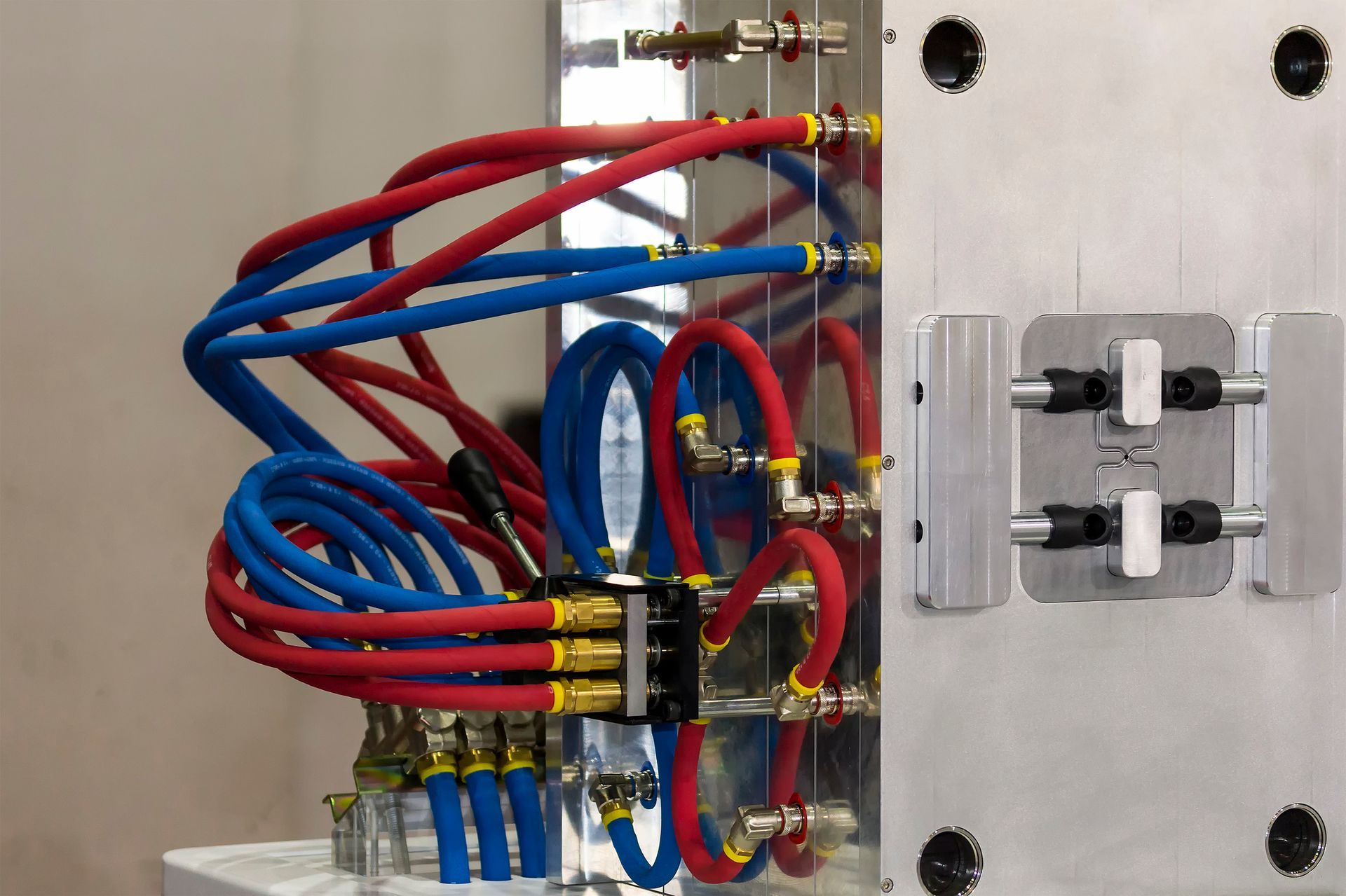 Close-up of a metal machine part with red and blue tubes connected to a black manifold. The tubes are bundled together.